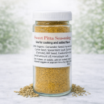 A clear glass jar of Sweet Pitta Seasoning with a white lid and white label, placed on a light marble surface with loose seasoning scattered around the base. The background is a soft, blurred white and green outdoor-style backdrop.